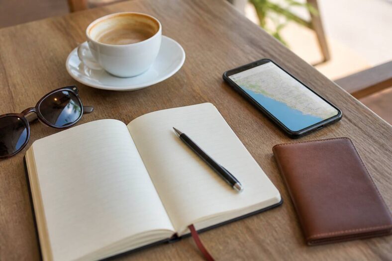 Notitieboek en reisbenodigdheden op tafel tijdens het plannen van een vakantie